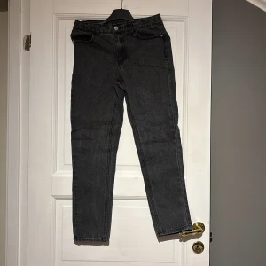 Svarta jeansbyxor - Snygga svarta jeansbyxor med en klassisk straight passform. De har en hög midja och är perfekta för en stilren look. Byxorna har fem fickor och stängs med dragkedja och knapp.
