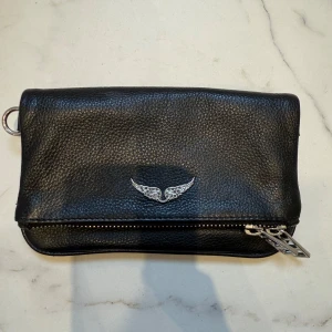 Zadig väska  - Jättesnygg Zadig väska i nyskick! Det är modellen Rock nano, alltså den mindre modellen. Nypris ca 3000 kr. Väskan kan bäras som en clutch men kommer även med en kedja. 