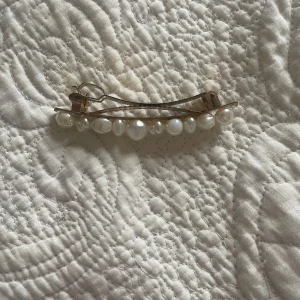 Hårspänne med pärlor - Elegant hårspänne i guld med vita pärlor. Perfekt för att ge en stilfull touch till din frisyr. Pärlorna är jämnt placerade längs spännet och ger en klassisk look.