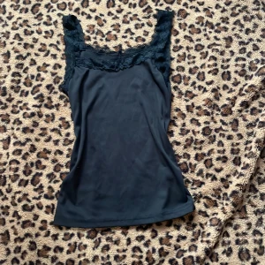 Svart linne med spetsdetaljer - Snygg svart linne med spetsdetaljer vid axlarna och halsringningen. Perfekt för att lägga till en touch av elegans till din outfit. Passar bra till både jeans och kjol. passar som M skulle jag säga
