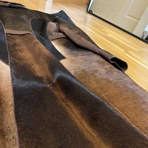 Brun pälsjacka med bälte - Snygg brun pälsjacka med en lyxig känsla. Jackan har en dubbelknäppt design med stora knappar och ett bälte i midjan. Den har en elegant krage och långa ärmar. Perfekt för att hålla sig varm och stilren. Köptes för 15,000kr