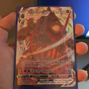 Coalosal VMAX Pokémonkort - Säljer ett Coalosal VMAX Pokémonkort med 330 HP. Kortet har attacker som Eruption Shot och G-Max Boulder. Det är en del av VMAX-serien och har en färgglad design med en bild av Coalosal i Gigantamax-form.