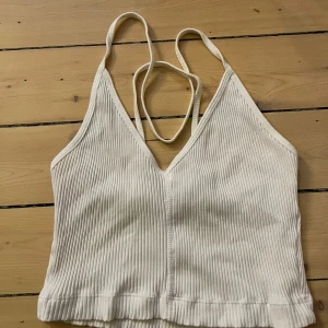 Vit ribbat linne från Zara - Säljer en stilren vit ribbad topp från Zara. Toppen har smala axelband och en djup v-ringning och är korsad i ryggen. Perfekt att ha som det är eller under en tröja/kofta. Aldrig använt. Pris kan diskuteras!☺️