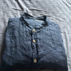 Mörkblå linneskjorta från Forex - Säljer en stilren mörkblå skjorta i linne från Forex. Skjortan har långa ärmar och knappar framtill. Perfekt för en avslappnad men ändå elegant look. Passar bra till både jeans och chinos.