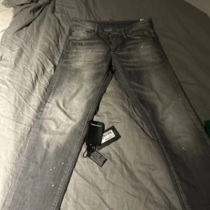 Grå jeans från Dsquared2 - Snygga grå jeans från Dsquared2 med en cool tvättad look och små vita färgstänk. De har en klassisk femficksdesign och knappgylf. Perfekta för en trendig och avslappnad stil.