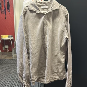 Beige skjorta - Snygg grå långärmad skjorta från Eton med klassisk krage och knappar framtill. Perfekt för en stilren look. Skjortan har en diskret randig textur som ger den en extra touch av elegans.