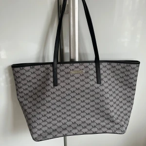 Svart/grå shoppingväska från Michael Kors - Michael Kors Emry large tote bag. Snygg och rymlig shoppingväska/tote/weekendväska från Michael Kors med det klassiska MK-mönstret. Väskan har svarta handtag och en praktisk dragkedja upptill. Perfekt för att bära med sig allt man behöver under dagen. Helt ny och oanvänd. Bredd 50x30cm. Äkta med lappar kvar