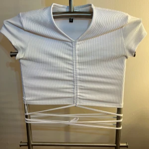 Vit ribbad topp från H&M Divided - Säljer en snygg vit ribbad topp från H&M Divided. Toppen har korta ärmar och en knytning framtill som ger en cool look. Perfekt för en avslappnad stil.