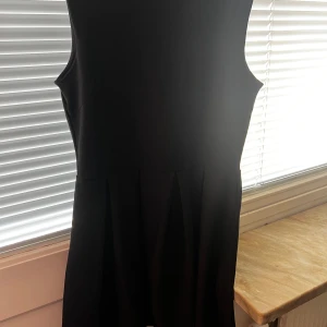 Svart ärmlös klänning från Rut m.fl. - Snygg svart ärmlös klänning från Rut m.fl. Perfekt för en stilren look. Klänningen har en dragkedja i ryggen för enkel påklädning. Passar bra till olika tillfällen och kan enkelt matchas med accessoarer.