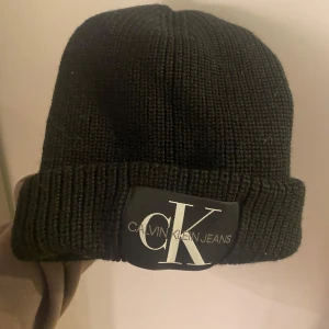 Svart stickad mössa från Calvin Klein Jeans - Snygg svart stickad mössa från Calvin Klein Jeans med en bred uppvikt kant och en stor logga framtill. Använd max 4 gånger🤍🤍