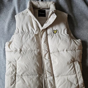 Vit dunväst från Lyle & Scott - Tjena tjena säljer en skön vit dunväst från Lyle & Scott med dragkedja och broderad logga på bröstet. Den är i storlek S, passar med det mesta i garderoben och perfekt för höst och vår.
