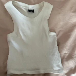 Vit ribbad linnetopp från Gina Tricot - Säljer en stilren vit ribbad linnetopp från Gina Tricot. Perfekt för varma dagar med sin ärmlösa design och mjuka material. Enkel att matcha med olika outfits.