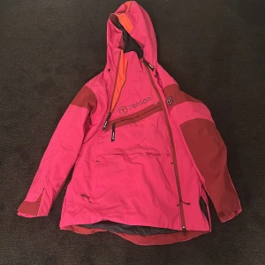 Rosa vindjacka från Tenson - Säljer en rosa vindjacka från Tenson med huva och dragkedja. Jackan har en cool design med mörkare rosa detaljer och en praktisk ficka på bröstet. Perfekt för utomhusäventyr och håller dig skyddad mot vinden.
