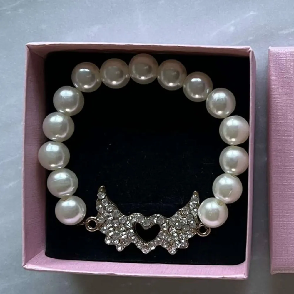 Elegant pärlarmband med en glittrig hjärtformad detalj i mitten. Armbandet består av vita pärlor och har en vacker design som passar perfekt för speciella tillfällen.. Asusteet.
