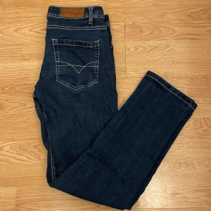 Mörkblå jeansbyxor från S.C.W - Snygga mörkblå jeansbyxor från S.C.W med klassisk femficksdesign och kontrastsömmar. Byxorna har en rak passform och är perfekta för en avslappnad stil. De har en knappgylf och bälteshällor för extra funktionalitet. Skriv om ni har funderingar och priset är inte hugget i sten!