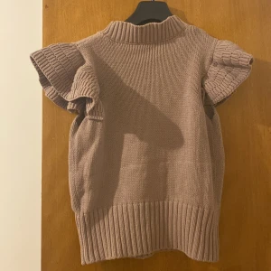 Beige stickad tröja - Säljer en mysig beige stickad tröja då den är för liten. Tröjan har korta ärmar och en ribbad krage samt nederkant. Knappt använd.