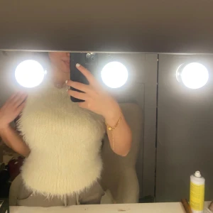 Vit ärmlös topp i pälsimitation - Säljer en fluffig vit ärmlös topp i pälsimitation. Toppen har en rund hals och är perfekt för att ge en trendig look. Passar bra till både jeans och kjol.