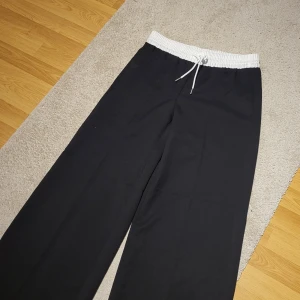 Svarta byxor med vit resårmidja - Snygga svarta byxor från HM med en kontrasterande vit resårmidja och snörning. Perfekta för en avslappnad stil med en loose passform.