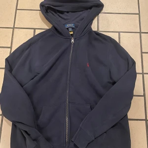 Mörkblå hoodie från Ralph Lauren (strl S) - Säljer en snygg mörkblå hoodie från Ralph Lauren med dragkedja. Den har tvättats många gånger och tappat lite av den blåa färgen. Ett okej använt skick.