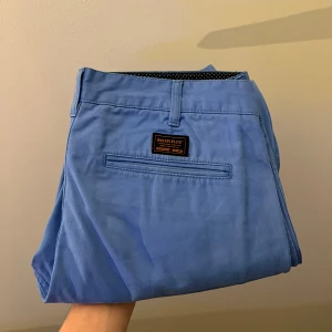 Blå chinos från Morris - Snygga blå chinos från Morris med en stilren design. Byxorna har en diskret prickig insida i midjan och en klassisk passform. Perfekta för en stilren look.