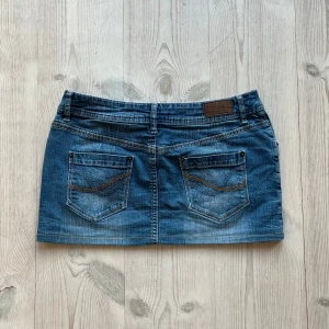 Blå lågmidjad jeanskjol  - Lågmidjad jeanskjol från John Baner som jag har sytt upp från en längre kjol. Fint skick. Står storlek 40, jag skulle säga M men att den även kan passa S. Tvärs över midjan är det ca 40 cm och längs med sidan är det ca 30 cm. Använd gärna köp nu!
