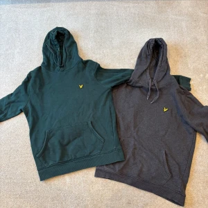 Grön och grå hoodie från Lyle & Scott - Två stilrena hoodies från Lyle & Scott i grönt och grått. Båda har en klassisk design med känguruficka och en liten gul logotyp på bröstet. Perfekta för en avslappnad stil.