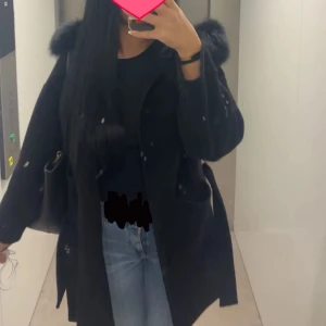 Svart kappa med pälskrage  - Snygg svart kappa med pälsdetaljer på kragen. Jackan har ett bälte i midjan för en justerbar passform 🌸
