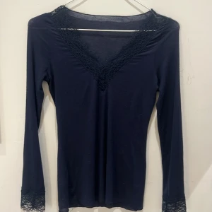 Mörkblå långärmad intimissimi tröja - Mörkblå långärmad tröja från intmissimi med v-ringning och spetsdetaljer vid hals och ärm. Mycket bra skick använt få tal gånger. Inga hål eller skavanker