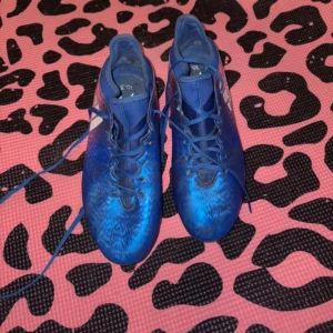 Blå fotbollsskor med snörning - Snygga blå fotbollsskor med snörning och ett coolt mönster. Perfekta för fotbollsplanen och ger bra grepp och kontroll. Skorna har en modern design och är bekväma att bära under långa matcher.