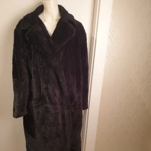 Svart pälsjacka - Säljer en elegant svart pälsjacka från PrettyLittleThing. Jackan har en klassisk design med långa ärmar och en mjuk, lyxig känsla. Perfekt för att hålla sig varm och stilren under kyliga dagar. ❗Kommer utan bälte. Det är håll under ena armen därav priset. Behöver tvättas. För fler bilder besök min Vinted sida
