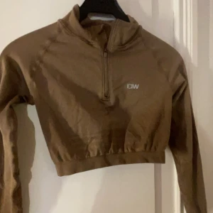 Brun croppad träningströja från ICANIWILL - Säljer en brun croppad träningströja från ICANIWILL. Tröjan har en halv dragkedja framtill och långa ärmar. Perfekt för träning och har en stilren design med logotyp på bröstet. Nyskick 