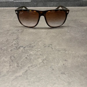 Bruna solglasögon från Ray-Ban - Snygga solglasögon från Ray-Ban med en klassisk brun sköldpaddsmönstrad båge. De har en stilren design med mörka glas och den ikoniska loggan på sidan. Perfekta för att ge en cool touch till din stil.