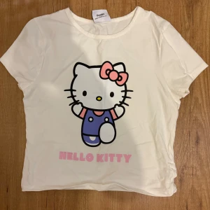 Vit Hello Kitty t-shirt - Säljer en söt vit t-shirt med Hello Kitty-tryck från Sanrio. T-shirten har korta ärmar och en rund halsringning. Perfekt för alla Hello Kitty-fans! 🐱🎀