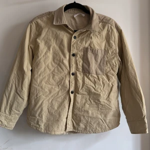 Beige over shirt från Zara  - Over shirt/ vårjacka med en bröstficka och svarta knappar. Skjortan har långa ärmar och en klassisk krage, yttertyget är creppat. Stl 152
