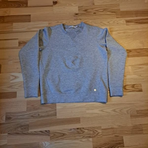 Grå tröja från Sail Racing - Säljer en stilren grå tröja från Sail Racing med ett subtilt mönster på framsidan. Tröjan har en v-ringad hals och långa ärmar, perfekt för en avslappnad look. Den är tillverkad i ett mjukt material som känns skönt mot huden.