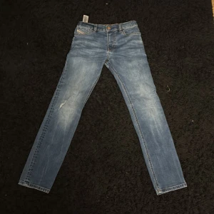 Blå jeans från Diesel - Snygga blå jeans från Diesel med klassisk femficksdesign och knappgylf. De har en lätt slitning på framsidan och en läderpatch med logotyp på baksidan. Perfekta för en avslappnad stil.