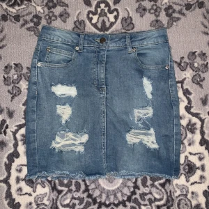 Blå jeanskjol - Snygg blå jeanskjol från Parisian med slitna detaljer och fransig nederkant. Kjolen har en klassisk femficksdesign och stängs med knapp och dragkedja 💕💕