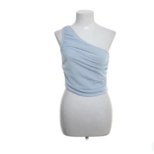 Ljusblå oneshoulder topp från NA-KD - Säljer en ljusblå oneshoulder topp från NA-KD. Toppen har endast använts ett fåtal gånger men har tyvärr fått lite små prickar på framsidan, men det är inget man tänker på när man har på sig den.