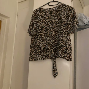 Leopardmönstrad blus med knyt - Säljer en leopardmönstrad blus med korta ärmar och knytning framtill. Blusen har en rund halsringning och är perfekt för att ge en trendig touch till din outfit. Materialet är mjukt och bekvämt.