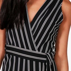 Svartvit randig omlottklänning - Snygg svartvit randig omlottklänning med knytband i midjan. Klänningen har en v-ringad design och är ärmlös, vilket ger en stilren look. Perfekt för en chic och modern stil. Vill helst max 100 kr