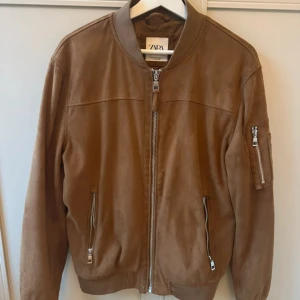 Brun bomberjacka från Zara - en snygg brun bomberjacka från Zara. Jackan har en dragkedja framtill och två fickor med dragkedjor. Den har en ribbad krage och ärmar samt en extra ficka på ärmen. 