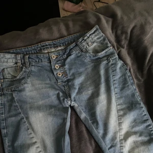 Blå snygga bootcut jeans!! - Snygga blå bootcut jeans med låg midja och klassisk femficksdesign. Jeansen har en ljus tvätt och snygga knappar framtill. Perfekta för en avslappnad stil. Supersnygga och väldigt lågmidjade❤️‍🔥❤️‍🔥 Storleken står tyvärr inte men skulle säga att dem passar S & M!! Priset går att diskutera💞