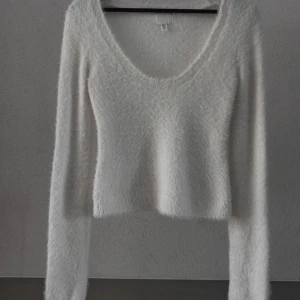 Vit fluffig tröja från H&M - Mysig vit tröja från H&M med fluffig textur och v-ringad hals. Perfekt för kyliga dagar med sin långärmade design. En stilren och bekväm tröja som passar till många tillfällen.