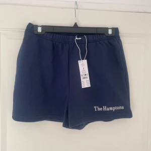 Mörkblå shorts med text - Snygga mörkblå shorts med texten 'The Hamptons' tryckt i vitt på ena benet. Perfekta för en avslappnad stil. 