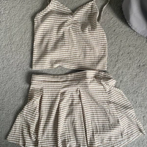 Beige och vit rutig kjol med matchande topp - Säljer en söt beige och vit rutig kjol med matchande topp. Kjolen har en kort längd och ett veckat mönster som ger en fin volym. Toppen är ärmlös med smala axelband. Perfekt för en somrig look! Aldrig använt💞💞