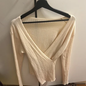 Beige ribbad omlottopp - Snygg beige ribbad omlottopp med långa ärmar. Perfekt för en stilren look. Den djupa v-ringningen ger en elegant touch. Passar bra till både jeans och kjol. Den är från SHEIN