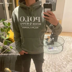 Grön Ralph Lauren hoodie - Tjena ! Säljer nu en snygg hoodie från Ralph Lauren med stor vit logga på framsidan. Den har en klassisk känguruficka och luva. Tröjan har inga skador eller defekter, då den är i nyskick. Kontakta för fler frågor eller bilder 🙌