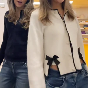 Kofta - Säljer en stilren vit kofta med svarta detaljer och söta rosetter vid fickorna. Koftan har långa ärmar och en klassisk rund halsringning. Perfekt för en chic och elegant look. Passar bra till både jeans och kjol.