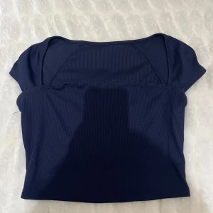 Mörkblå ribbad topp - Snygg mörkblå ribbad topp med korta ärmar. Perfekt för en stilren look. Toppen har en enkel design som gör den lätt att matcha med olika outfits.