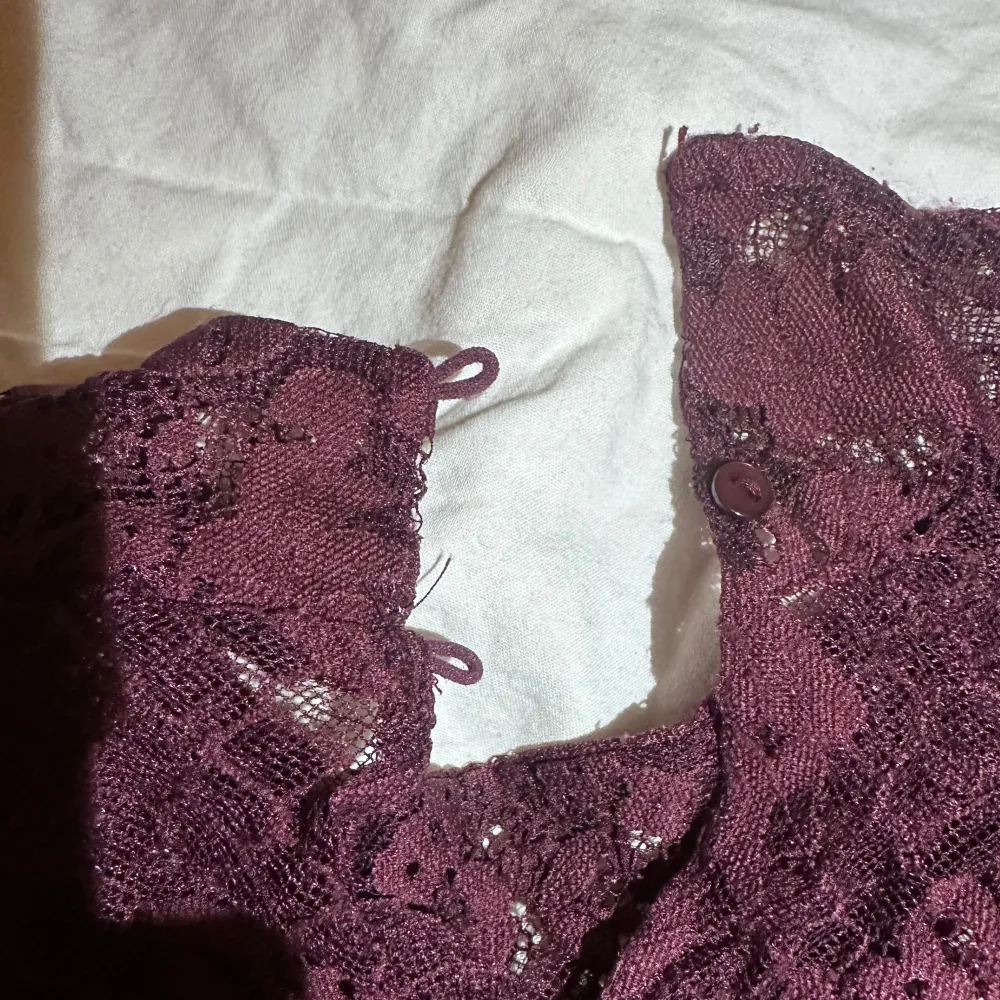Säljer en elegant vinröd spetsblus med långa ärmar och fina spetsdetaljer. Blusen har en hög hals och knappar i nacken för en stilren look. En knapp har låstnat. Köpare står för frakt . Puserot.
